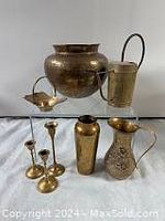 Front view of seven brass decorative items arranged on a white cloth.