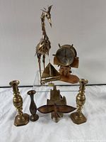 Wide shot showing full lot including brass candlesticks, brass vase, brass bird sculpture, sailboat figurine, wooden clock, and wooden carved piece.