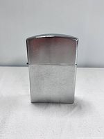 Front view of large silver-tone lighter with brushed body and polished top lid, standing upright on white surface