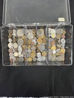 Top view of a transparent plastic organizer box filled with various coins sorted into compartments.