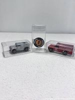 Front view of two Redline Hot Wheels cars in clear cases and a Mattel Hot Wheels metal cap in a display case arranged side by side