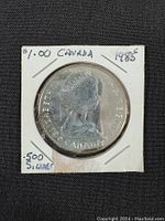 Obverse side of the 1985 Canadian silver dollar coin featuring Queen Elizabeth II's profile, in holder labeling it as $1.00 Canada and .500 silver.