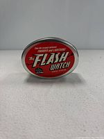 Photo of closed oval metal tin case with red top showing 'The Flash Watch' and DC Comics logos.