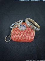 Lot contents showing two bangle bracelets resting on a red and gold patterned pouch from Thailand.