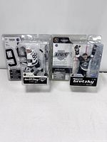 Front view of two Wayne Gretzky action figures in original packaging, one in white Edmonton Oilers uniform and one in black Los Angeles Kings uniform.