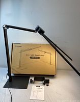 Fimei 2-in-1 LED desk lamp fully assembled next to original box, clamp attachment, and instruction manual on flat surface
