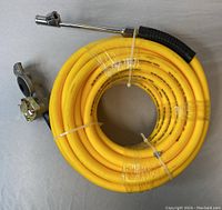 Coiled yellow air hose wrapped in plastic with attached inflation chuck and quick-connect fittings laid on a flat surface.