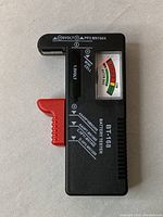 Front view of BT-168 battery tester showing analog meter, battery type labels, and sliding red grip