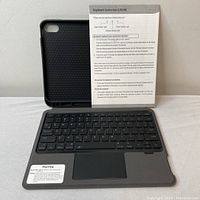Black Bluetooth keyboard integrated into a tablet case with a touchpad below the keys and an instruction sheet standing behind the case. The interior of the case has a honeycomb pattern.