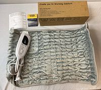 Photo showing full body heating pad with soft, quilted gray fabric, wired controller plugged in, product box, and instruction manuals.