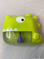 Front view of the green dinosaur bath toy showing the clear reservoir with water spinner inside.