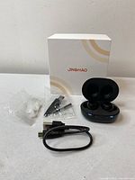 Box with earpieces charging case, USB cable, ear tips, and clip accessory laid out