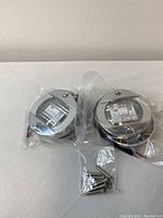 Two round LED boat lights in polished chrome-like metal housing, sealed in plastic, with metal screws for installation on white surface.