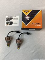 Photo of the B2 Series LED light bulb box with two metallic LED bulbs and installation guide on a white surface.