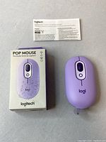 Top view showing purple Logitech Pop mouse next to its box and user manual on a neutral surface.