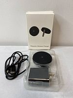 Magnetic wireless charger in plastic packaging alongside USB cable and power adapter, with white product box behind them.