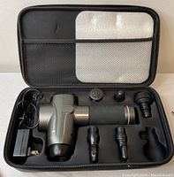 Open carrying case showing the massage tool, five different massage head attachments, and charger neatly placed in custom molded slots.