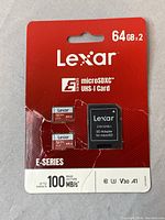 Front view of packaging showing two 64GB Lexar microSDXC E-Series cards and an SD adapter, highlighting 100 MB/s read speed and UHS-I interface.