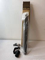 Microphone boom arm in plastic wrapping leaning against its box with mounting clamp and accessories placed in front.