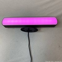 Front of the colored RGB light bar illuminated in pink/purple, showing diffuser panel and black housing with attached USB cable.