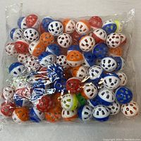 Clear plastic bag filled with approximately seventy small bell balls in assorted colors: white, blue, orange, red, and green. Balls are cage-shaped with multiple holes.