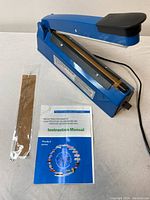 Blue plastic film sealer with a hinged black top sealing arm, powered by an electric cord, shown on white surface.