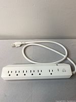 Top-down photo showing the full length of the white power bar with six AC outlets and four USB ports on top, along with the attached power cord.
