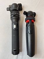 Photo of two Mobifoto selfie sticks with tripod and Bluetooth remote in black, showing textured grips and adjustable phone mounts.