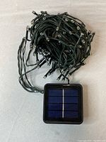 Coiled solar-powered Christmas string lights with attached solar panel on grey surface.