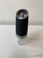 Front view of a battery powered spice grinder showing stainless steel grinding mechanism and clear container