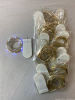 Ten sets of battery operated Christmas string lights with white battery packs and silver wire, some coiled, arranged on a surface.