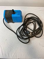 Blue and black submersible water pump with attached power cord coiled beside it, placed on a white surface.