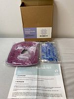 Photo showing therapeutic gel bead face mask set with box, pink and blue gel bead packs, and instruction sheet laid on table.
