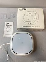 Yikhom wall-mounted soap dispenser with power cable connected, displayed with original box and instruction manual.