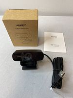 Webcam alongside its packaging box and user manual on a flat surface