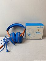 Front view of wired over-ear blue and orange headphones beside the box showing model AT 3