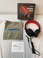 Headphones with carrying pouch and user manual laid out on the floor, showing packaging box and all included items