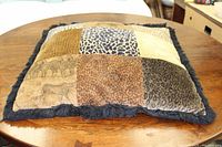 Top view of the throw pillow showing the patchwork of animal prints including leopard, cheetah, and zebra patterns with black fringe trim.