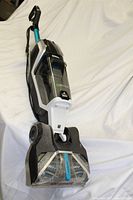 Front side view of Bissell JetScrub Pet carpet cleaner showing brush head, handle, and overall upright design in black, white, and teal colors.