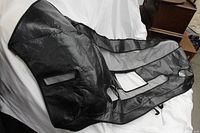 Black leather car bra displayed against a white cloth backdrop show front and mesh ventilation details.