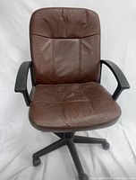 Front view of brown faux leather office chair with creased and worn seat and backrest, black plastic armrests, and black wheeled base.