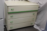 Full view of the creamy white chest of drawers with green accents on handles and top drawer stripe, showing the overall structure and condition.