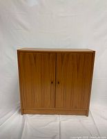 Front view of the compact wooden cabinet with closed double doors showing warm natural wood finish and small round handles