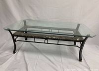 View of entire coffee table showing clear glass top, black metal frame, and marble accent beneath the glass surface