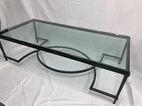 Side-angle view showing clear glass top and black metal base with circular and linear geometric pattern.