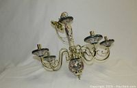 Photo of the full chandelier suspended against a white background showing its 5 arms with porcelain candleholders and brass accents.