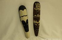 Photo showing two handcrafted tribal wooden wall masks side by side against a neutral background. The masks feature distinct tribal patterns in black, beige, and brown tones with carved details.
