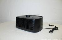 Side-angle view showing the elongated rectangular black compact air purifier with air vent grills and power cord.