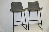 Pair of modern barstools with gray faux-leather seats and black metal frames, front view showing seat shapes and legs.