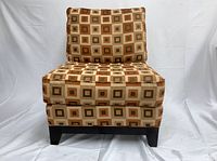 Front view of one of the two armless chairs showing the geometric square upholstery in shades of brown, beige, and orange with dark wood legs.